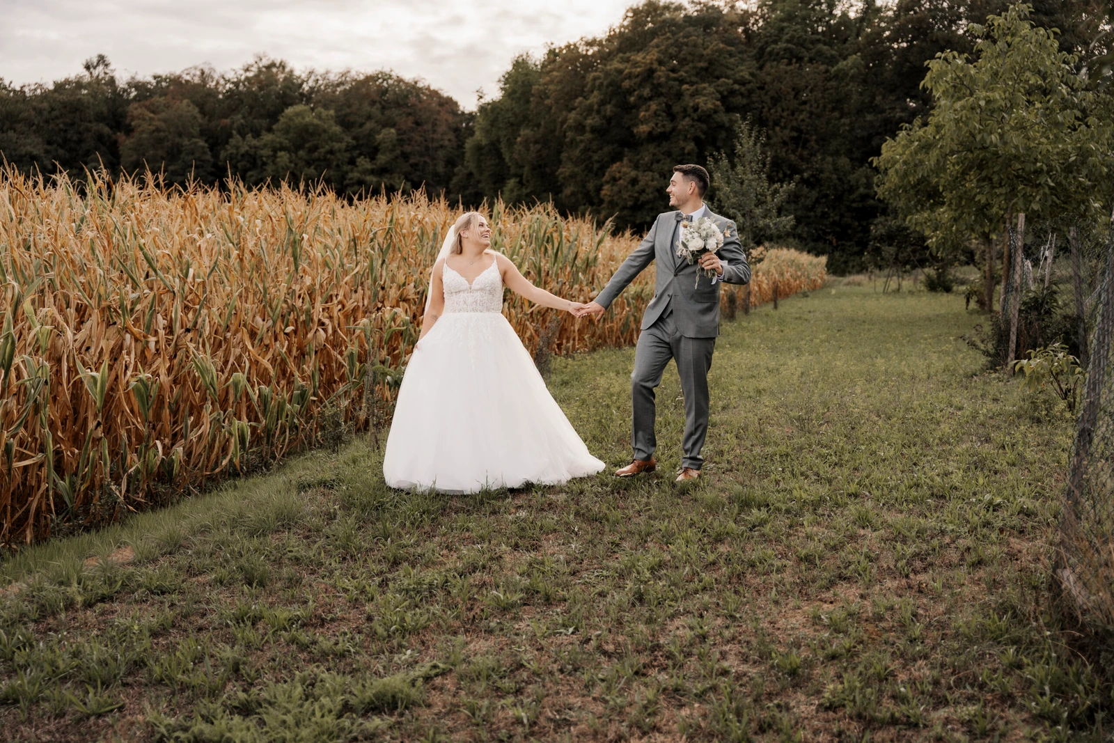 Laura und Philipp halten sich beim Paarshooting am Rand eines Maisfeldes an den Händen.