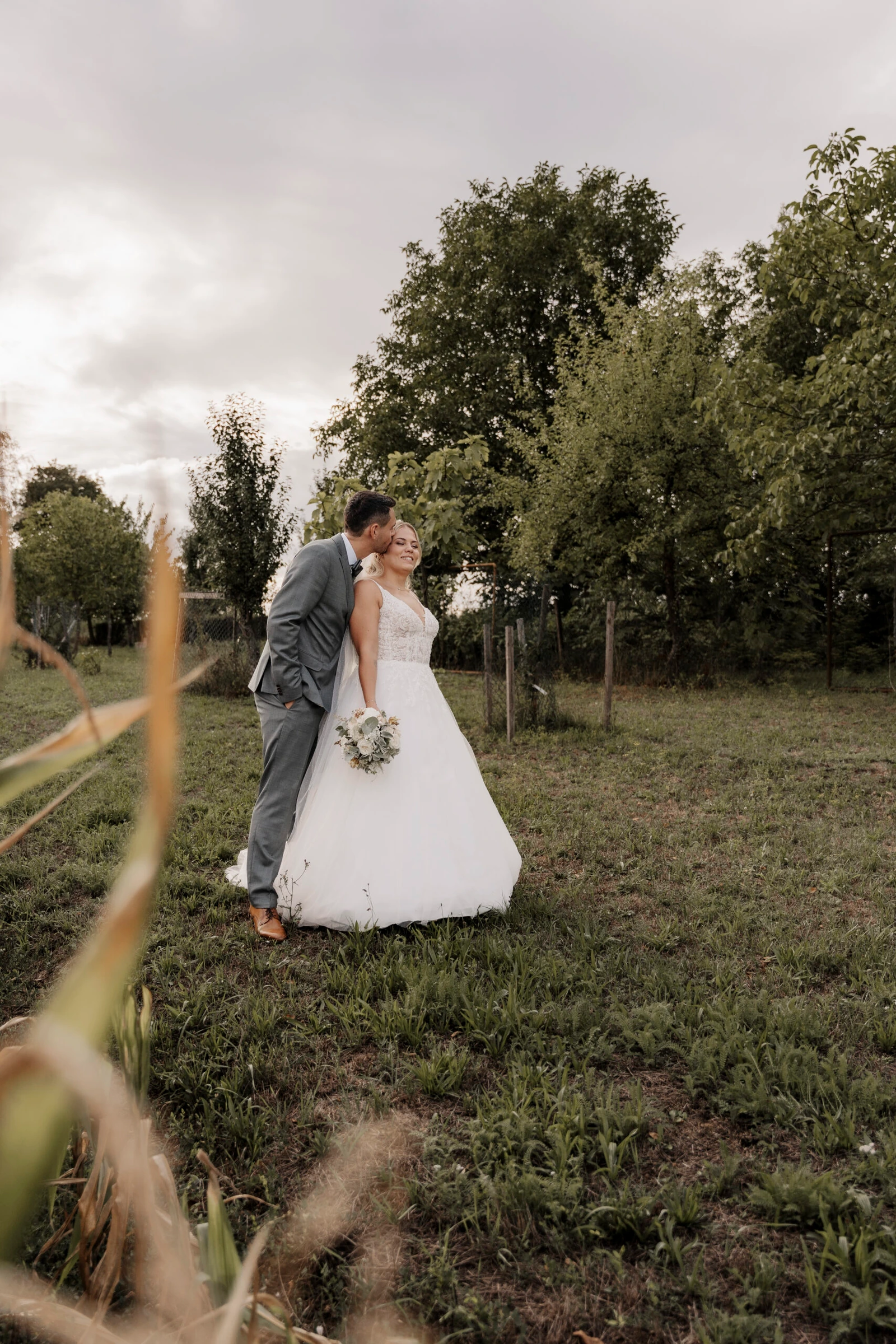 Laura und Philipp küssen sich auf einer Wiese, im Vordergrund stehen hohe Gräser.